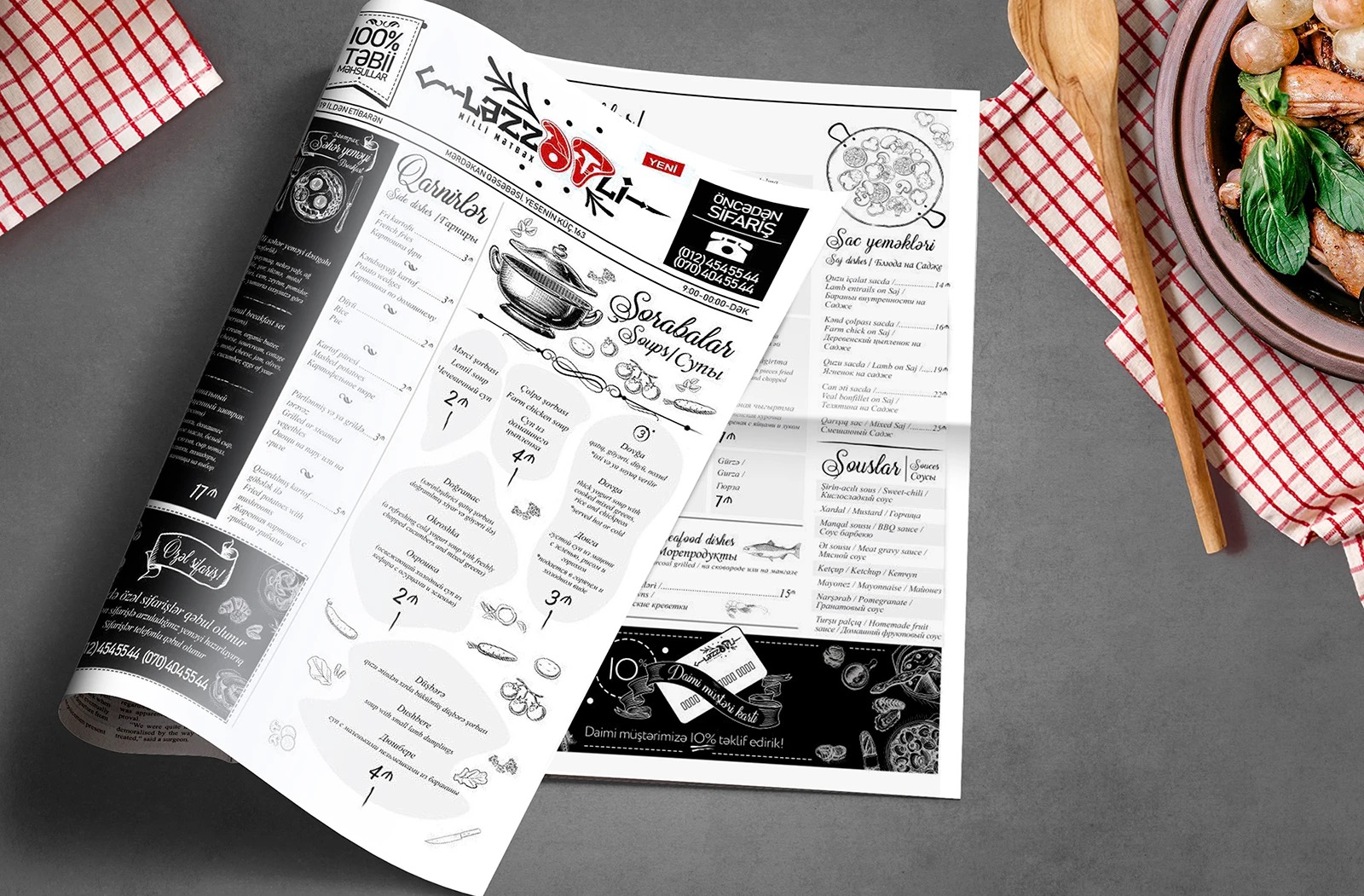 The printed menu folded on a grey table with a checkered napkin, wooden spoon and a clay plate of food