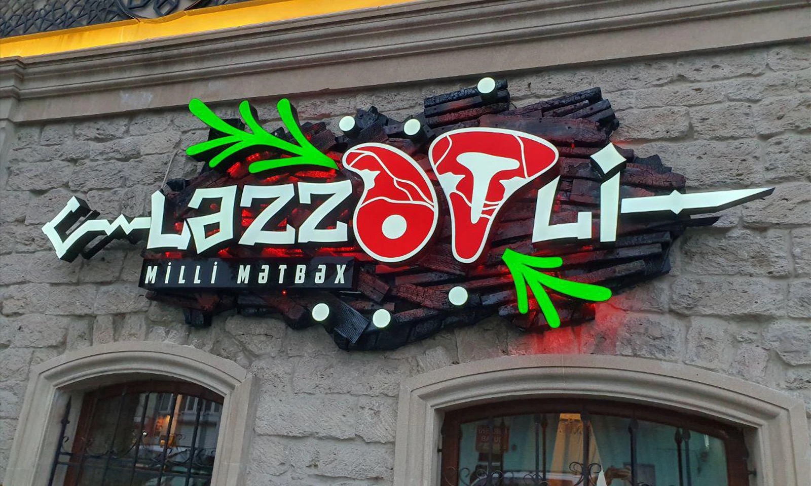 The fabricated Lezzetli sign on the stone facade by day: steel letters, red steaks, green herbs